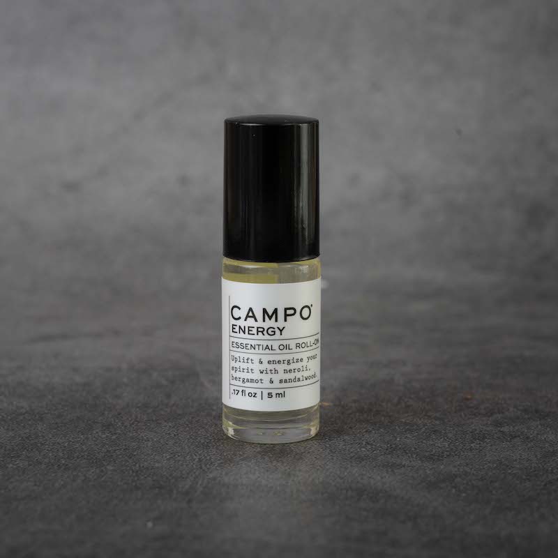 A small clear glass bottle with a white label. The label reads "CAMPO Energy Essential Oil Roll-on, Uplift & energize your spirit with neroli, bergamot & sandalwood, .17 fl oz, 5 ml". The bottle has a black twist-off lid.