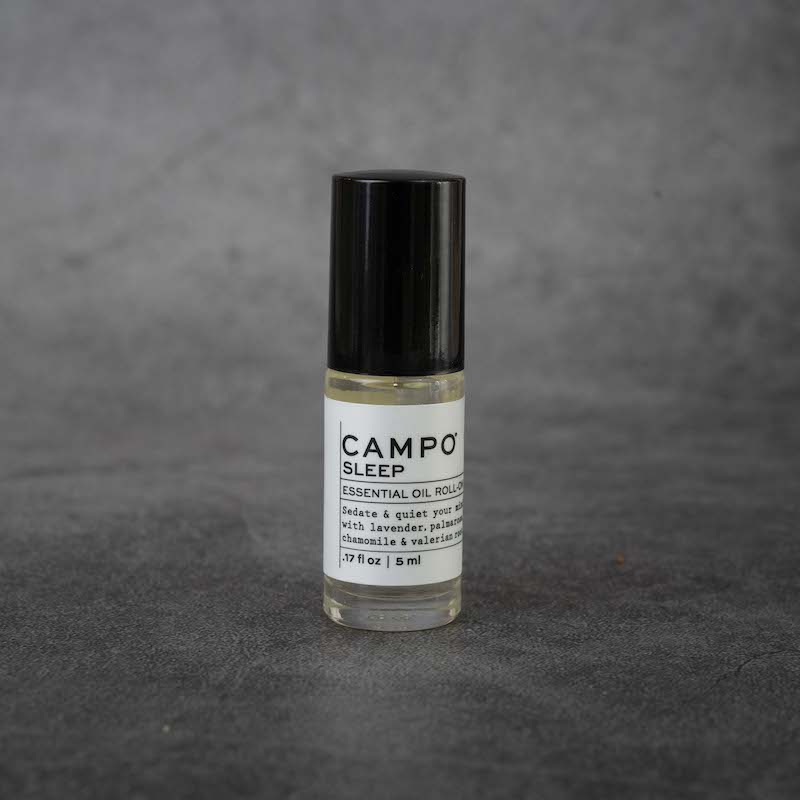 A small clear glass bottle with a white label. The label reads "CAMPO Sleep Essential Oil Roll-on, Sedate & quiet your mind with lavender, palmarose, chamomile & valerian root, .17 fl oz, 5 ml". The bottle has a black twist-off lid.