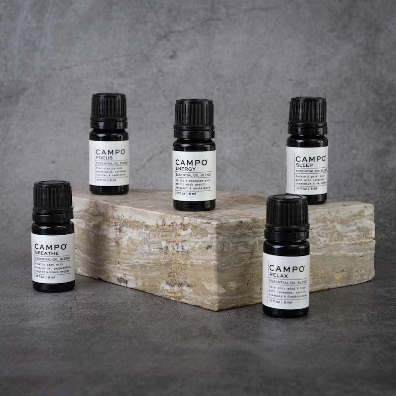 The full CAMPO Essential Oil Blend line. From left to right: Breathe, Focus, Energy, Relax, Sleep. All blends are in matching small black bottles.