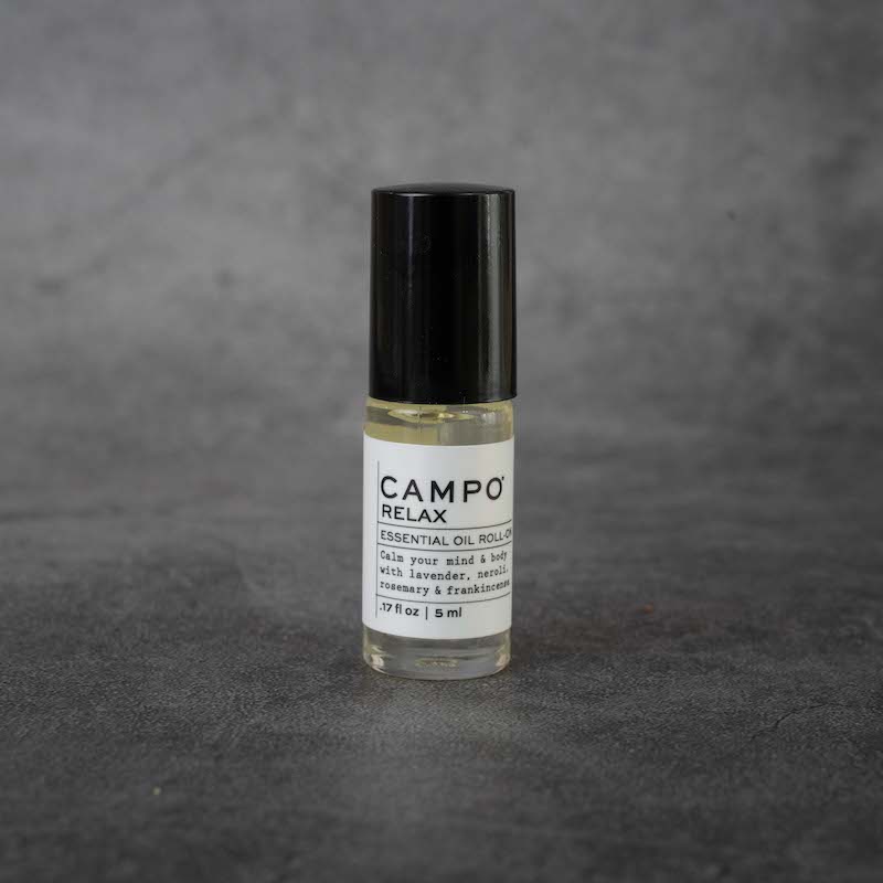 A small clear glass bottle with a white label. The label reads "CAMPO Relax Essential Oil Roll-on, Calm your mind & body with lavender, neroli, rosemary & frankincense, .17 fl oz, 5 ml". The bottle has a black twist-off lid.
