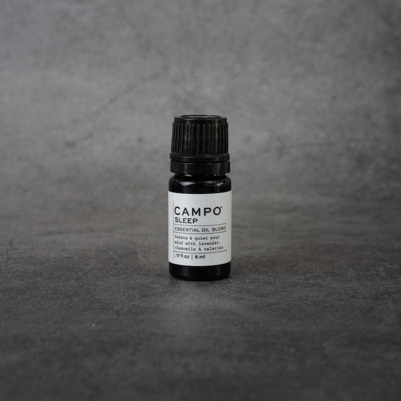 A small black bottle with a white label. The label reads "CAMPO Sleep Essential oil blend, Sedate & quiet your mind with lavender, chamomile & valerian, .17 fl oz, 5 ml" in black text. The bottle has a black twist-off lid.