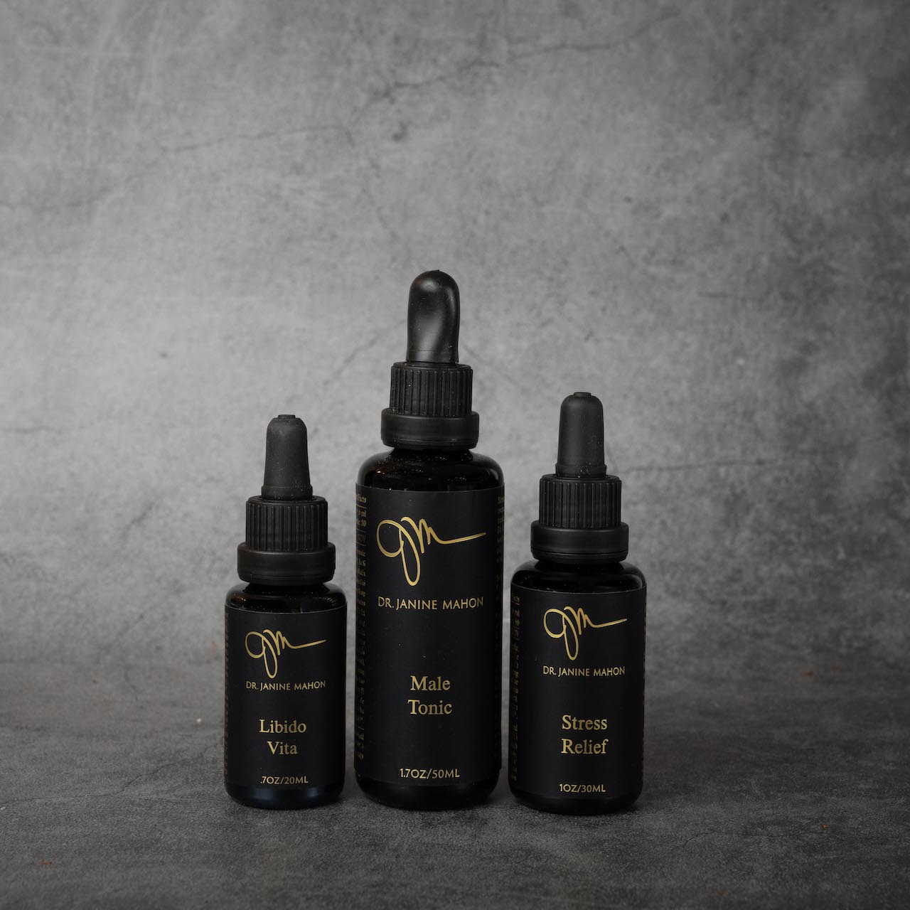 Three black bottles with gold lettering next to each other. The first bottle reads "Libido Vita", the second "Male Tonic", the third "Stress Relief". These three bottles are the full line of Dr. Janine Mahon products.