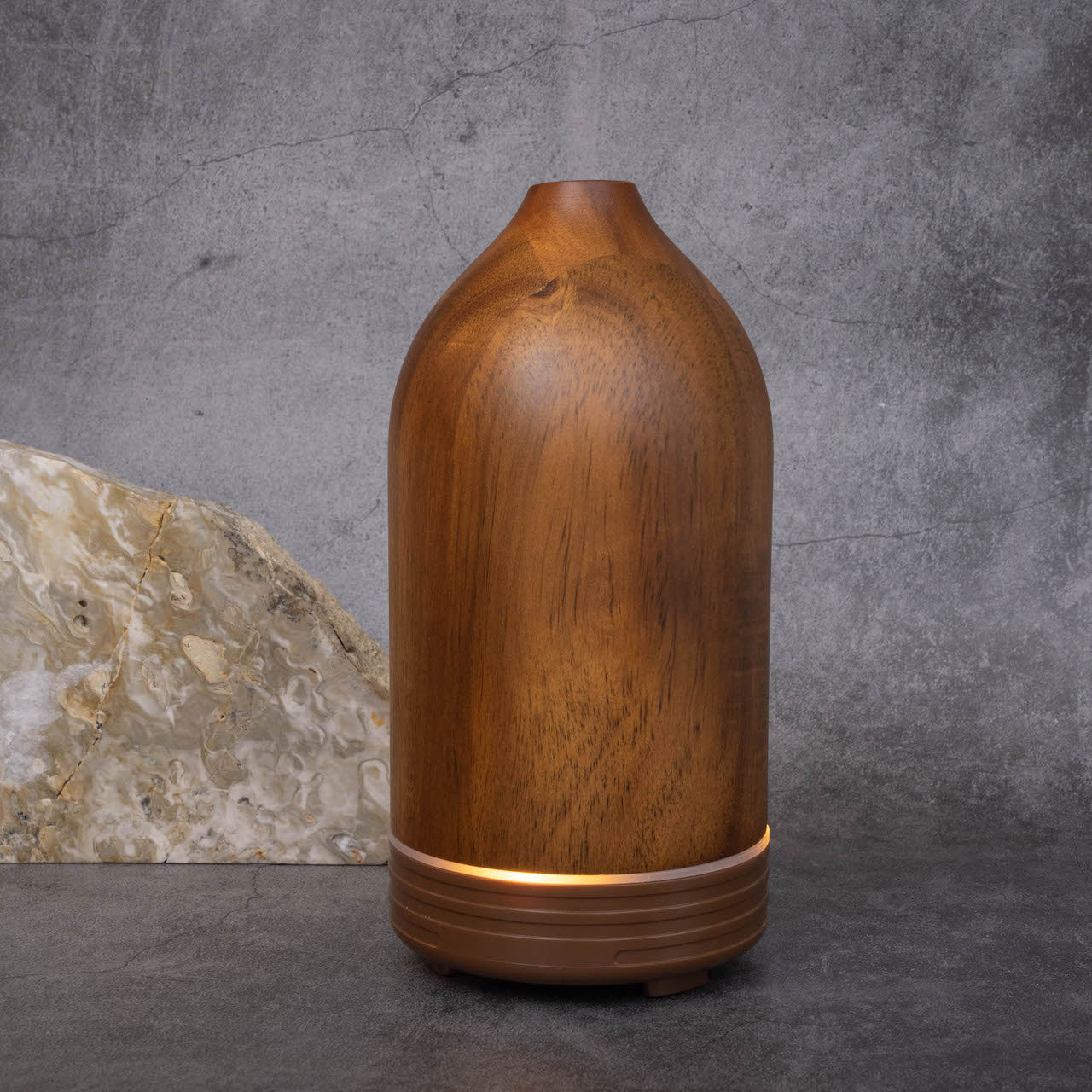 A cone-shaped dark wooden essential oil diffuser. There is band of light around the bottom indicating it has been turned on.