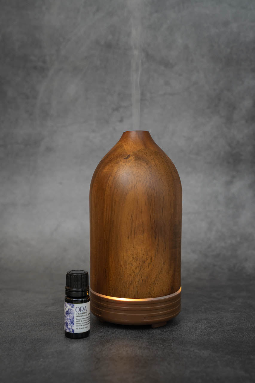 The same wooden diffuser as in the previous photos, with a small bottle of ORA by Campo essential oil blend.