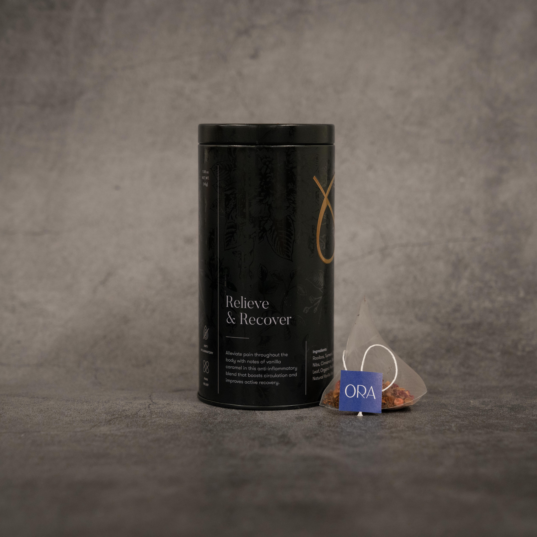 On the left, a black metal cylinder tin of tea reading "Relieve & Recover". On the right, a translucent tea bag with a string printed with the ORA logo.