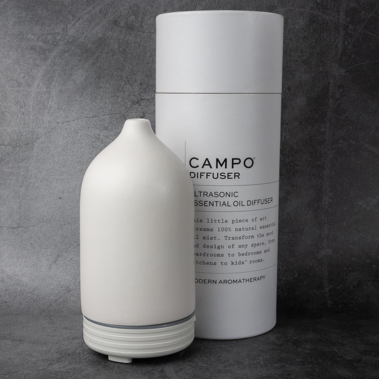 A white, cone shaped oil diffuser and a larger cylinder-shaped package reading "CAMPO Diffuser, Ultrasonic Essential Oil Diffuser" against a gray stone background.